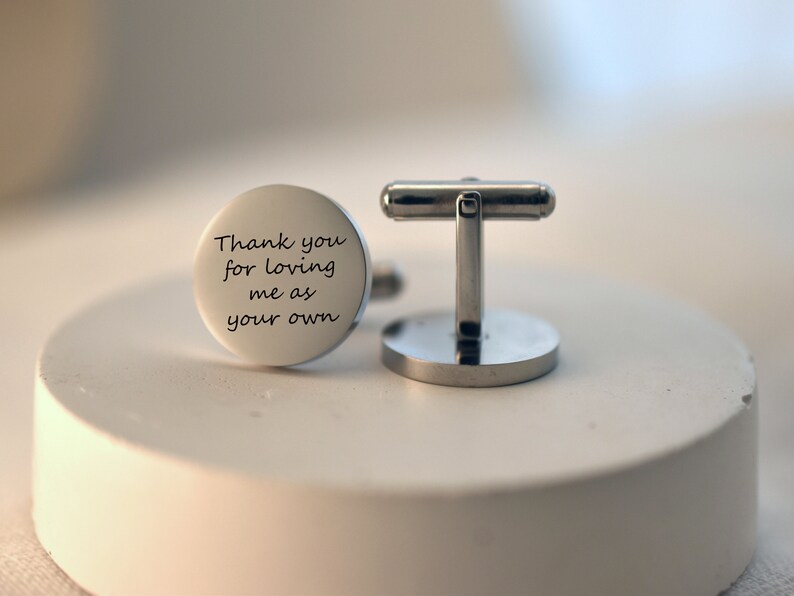 May include: Silver cufflinks with a round, engraved message that reads "Thank you for loving me as your own".