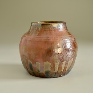 Peut inclure: Un petit vase rond en céramique avec un glaçage brun, rose et or. Le vase a un bord légèrement évasé et un fond arrondi.