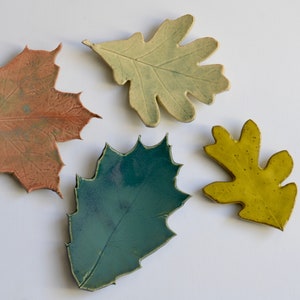 Op de afbeelding: Vier keramische bladeren in verschillende kleuren. De bladeren zijn lichtbruin, teal, geel en lichtgroen.