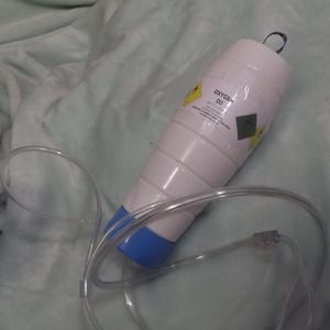 May include: A white oxygen tank with a blue cap and a clear plastic tube. The tank has a yellow warning label that says "Oxygen O2".