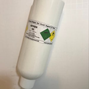 May include: A white oxygen cylinder with a blue string attached to the top. The cylinder has a label that says "Oxygen O2" and includes safety warnings.