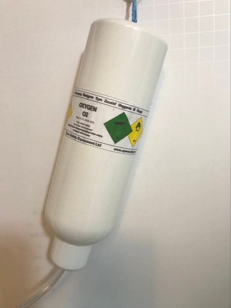 May include: A white oxygen cylinder with a blue string attached to the top. The cylinder has a label that says "Oxygen O2" and includes safety warnings.