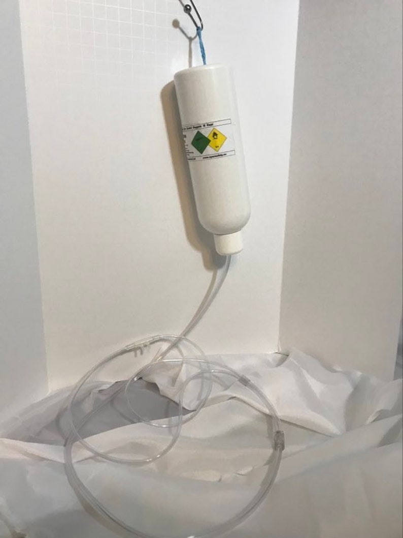 May include: A white cylinder with a blue and green label hanging from a hook. The cylinder is connected to a clear plastic tube.
