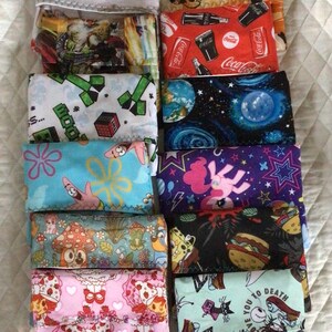 May include: A collection of colorful fabric pouches with various patterns. Designs include cartoon characters, space, Coca-Cola logos, and Halloween themes. Some pouches have text that reads "LOVE YOU TO DEATH".