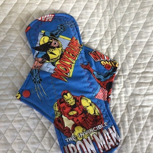 Könnte beinhalten: Blauer Stoffunterleger mit Superhelden-Motiv. Der Unterleger zeigt Bilder von Wolverine, Spider-Man und Iron Man. Der Text "The Invincible Iron Man" ist auf dem Unterleger aufgedruckt.