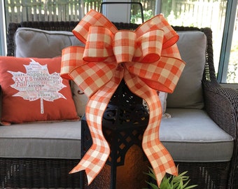 May include: A large orange and white checkered bow tied around a black lantern. The lantern is sitting on a table with a teal and orange pumpkin and a potted succulent plant.