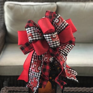 Puede incluir: Un lazo de cuadros rojos y negros con una cinta roja y una cinta a cuadros blancos y negros con un diseño de camión rojo. El lazo está atado alrededor de una linterna negra.