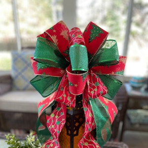 May include: A red and green Christmas bow with a gold glitter design. The bow is tied around a lantern.