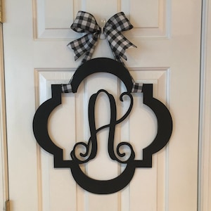 May include: Black wooden door hanger with a decorative, ornate frame and the letter "A" in a script font. The hanger is adorned with a black and white checkered bow.