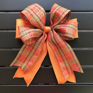 Könnte beinhalten: Eine große Schleife aus orangefarbenem und rotem kariertem Stoff mit einer mittleren Schlaufe. Die Schleife ist aus einem weichen, strukturierten Stoff gefertigt.