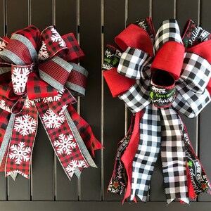 以下が含まれることがあります： 赤と黒のバッファローチェックのリボンを使ったクリスマスボウが2つ。1つは白い雪片、もう1つは緑と白のホリデー柄です。