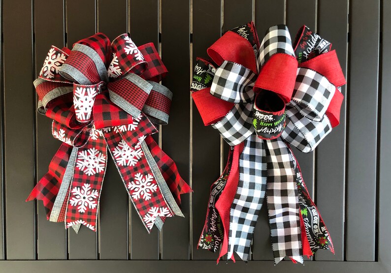 以下が含まれることがあります： 赤と黒のバッファローチェックのリボンを使ったクリスマスボウが2つ。1つは白い雪片、もう1つは緑と白のホリデー柄です。