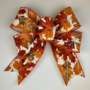 May include: A large, orange and white bow with a leaf pattern. The bow is made of fabric and has a satin finish.