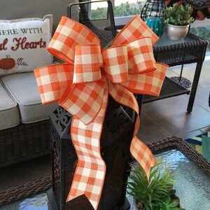 May include: A black metal lantern with an orange and white checkered bow. The lantern has a decorative design and is sitting on a table.