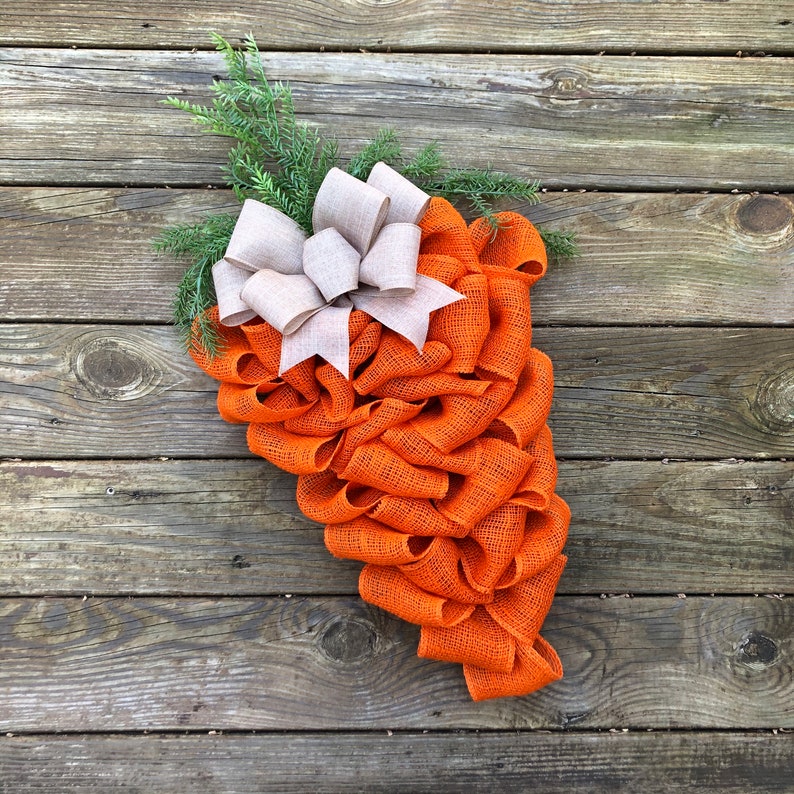 May include: Orange burlap wreath with a large white bow. The wreath is shaped like a carrot and is perfect for a spring or summer door decoration.