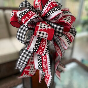 以下が含まれることがあります： バッファローチェック柄の赤、白、黒のクリスマスリボンに、「メリークリスマス」と「メリー」の文字が書かれたリボン。黒いランタンに結ばれています。