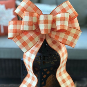 May include: A large orange and white gingham bow with a wired edge. The bow is tied around a black lantern.