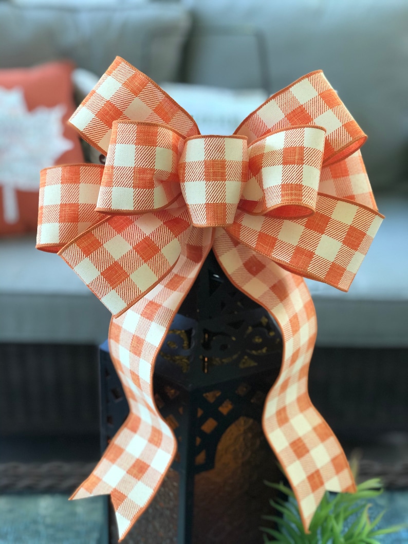 May include: A large orange and white gingham bow with a wired edge. The bow is tied around a black lantern.