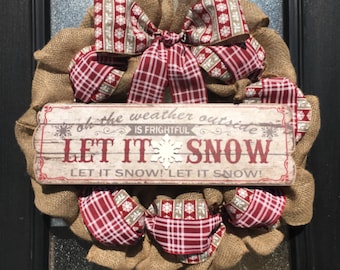 May include: A burlap wreath decorated with a red and white checked ribbon and a sign that reads "Oh the weather outside is frightful, Let it snow! Let it snow! Let it snow!"