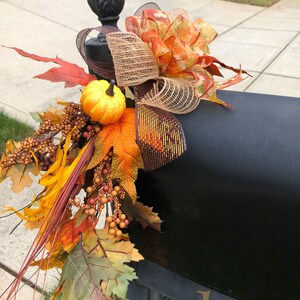 May include: A black mailbox decorated with fall-themed accents. The arrangement includes a decorative bow with orange and brown ribbons, faux pumpkins, and colorful fall leaves. The mailbox has the number 1032 in gold.