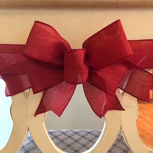 May include: A large, burgundy bow made of a textured fabric is tied around a white, decorative railing.