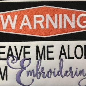 May include: Embroidered patch with the text "WARNING" in white on an orange hexagon, above "LEAVE ME ALONE I'M Embroidering" in black and purple script. A small pink flower is near the word "Embroidering".