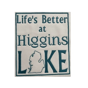 May include: Embroidered rectangular patch with the text "Life's Better at Higgins Lake" in teal. The word "Lake" is below a teal outline of the state of Michigan. The patch is on a white background.