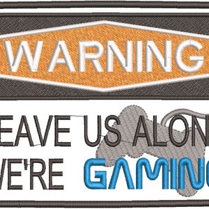 Puede incluir: Parche bordado con borde negro. Dice "WARNING" encima de "LEAVE US ALONE WE'RE GAMING". La palabra "GAMING" está en azul, e incluye un gráfico de mando gris.