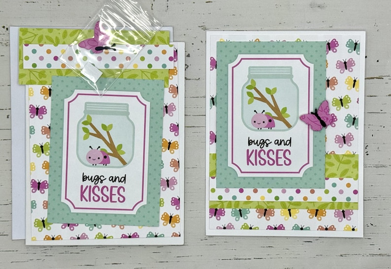 May include: Two handmade greeting cards with a green, white, and pink color scheme. The cards feature a jar with bugs and the text "bugs and kisses".