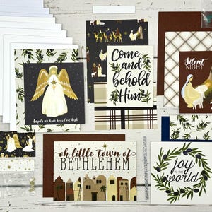 May include: A set of Christmas card making supplies featuring a variety of patterned paper, cardstock, and embellishments. The paper includes designs with angels, stars, olive branches, and a town scene. The text on the paper includes "Come and behold Him", "Silent Night", "oh little town of BETHLEHEM", and "joy to the world".