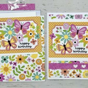 May include: Two handmade greeting cards with a floral and butterfly design. The cards are yellow, pink, and green with the text "happy birthday".