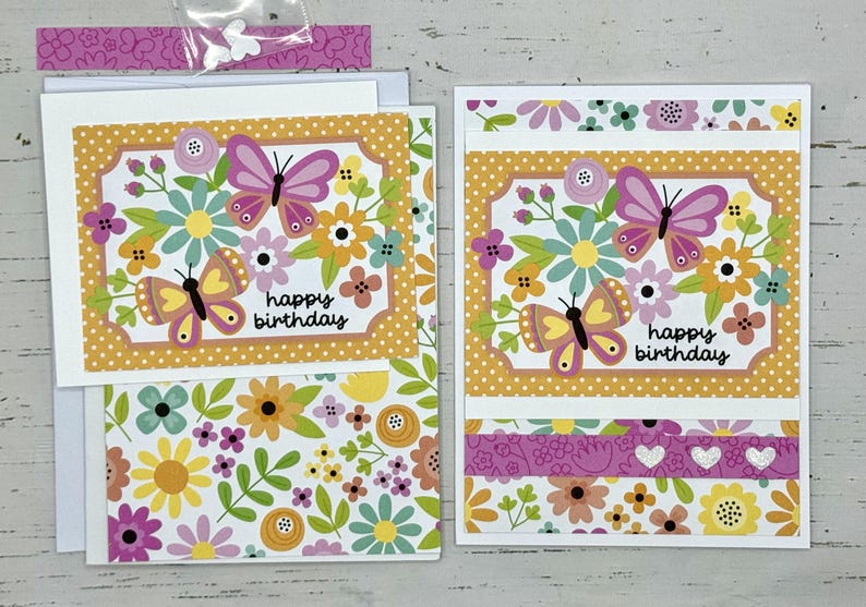 May include: Two handmade greeting cards with a floral and butterfly design. The cards are yellow, pink, and green with the text "happy birthday".