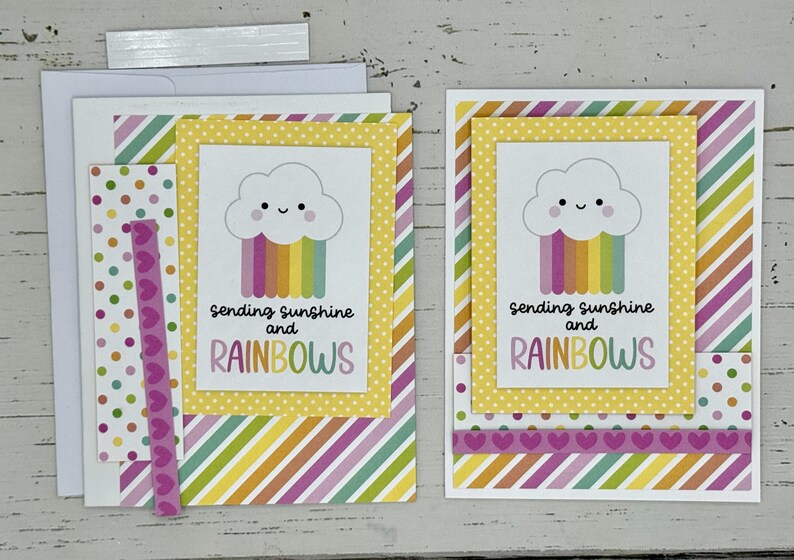 May include: Two handmade greeting cards with a yellow, white, and rainbow cloud design. The cards feature the text "Sending sunshine and rainbows".