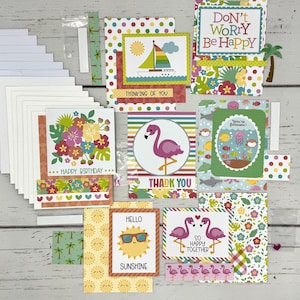 May include: A collection of colorful greeting cards with tropical themes. Designs include a sailboat, flamingo, and sun with sunglasses. Text on the cards reads "Thinking of You", "Don't Worry Be Happy", "Happy Birthday", "Thank You", "Hello Sunshine", and "So Happy Together".