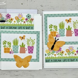 May include: Two handmade greeting cards with a green and white polka dot border. The cards feature a floral design with potted plants and butterflies. The text on the cards reads "Life is but a dream".