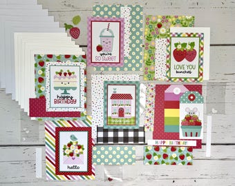 May include: A collection of greeting cards and stationery with a strawberry theme. The cards feature illustrations of strawberries, cakes, and other cute designs. The color palette includes pink, red, green, and white. Some cards have text that says "Happy Birthday" and "Love You bunches".