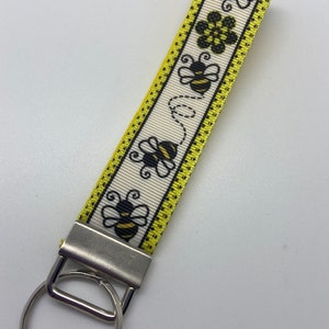May include: A white and yellow key chain with a black and yellow bee design. The key chain has a silver key ring.