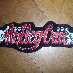 May include: Red embroidered "Motley Crue" patch with white skull and crossbones on a black background.