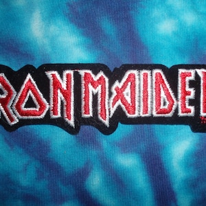 Puede incluir: Parche de logotipo de la banda Iron Maiden con letras bordadas en rojo sobre fondo negro.