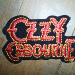 Może przedstawiać: Czarna łatka z tkaniny z czerwonym i złotym haftem. Łatka zawiera napis "ZZY  ZBOUBNE".