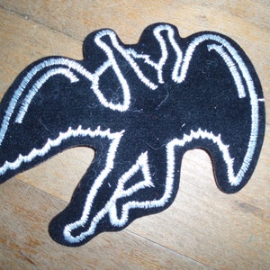 May include: Black felt patch with a white outline of a bird with wings spread. The bird is in a flying position.