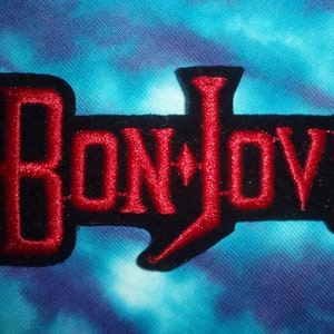 Puede incluir: Parche bordado "Bon Jovi" en rojo con contorno negro y símbolo de marca registrada.
