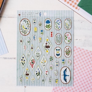 May include: A sheet of decorative stickers with various floral and animal designs. The stickers feature oval and diamond shapes with images of birds, flowers, butterflies, and deer. The background is a light blue with vertical stripes. Text at the top reads "birds song x seal deer dream".