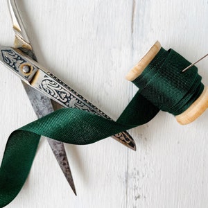 May include: A spool of dark green ribbon with a pin, and a pair of antique silver scissors.