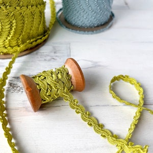 May include: A spool of yellow scalloped trim with a wooden bobbin. The trim is on a white surface.