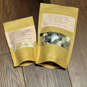 May include: Two brown paper bags of Dayton's Fluffy Homestead dehydrated rabbit hide bites for dogs and cats. The bags have a clear window showing the contents. Text on the bags includes "Dehydrated Rabbit Hide Bites" and "For Dogs & Cats | Not for Human Consumption."