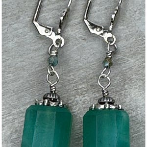 May include: Dangle earrings featuring teal, rectangular beads with a faceted design. The earrings have silver-coloured lever-back closures and decorative silver accents. The text "The Salvaged Bead" is at the top.