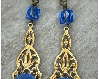 Könnte beinhalten: Ein Paar Ohrhänger mit goldfarbenem Filigran-Design. Jeder Ohrring hat eine blaue, rechteckige, geschnitzte Perle und eine blaue Kristallperle. Der Text "The Salvaged Bead" steht oben.