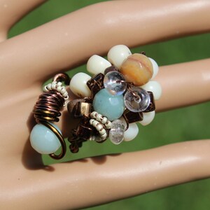 May include: A copper wire ring with a cluster of white, brown, and blue beads. The beads are arranged in a flower-like shape.