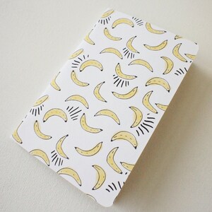 Puede incluir: Un cuaderno rectangular con fondo blanco y un patr&oacute;n repetido de pl&aacute;tanos amarillos con detalles negros. Los pl&aacute;tanos est&aacute;n en varias orientaciones, creando un dise&ntilde;o l&uacute;dico. El cuaderno tiene esquinas redondeadas.